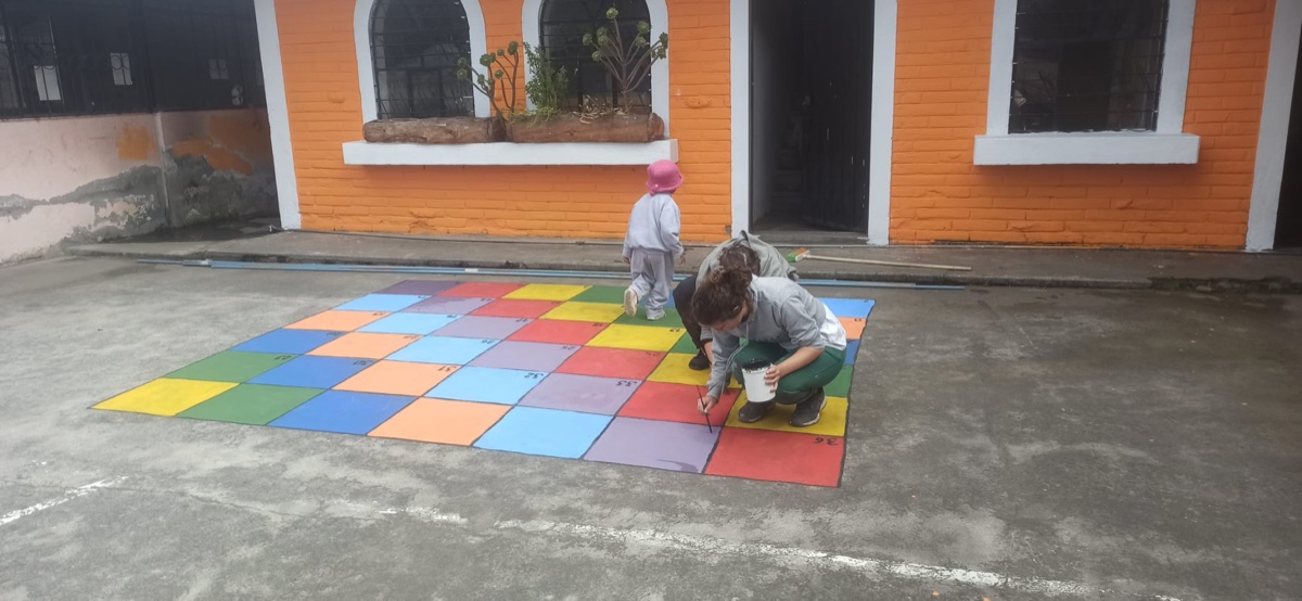 Volunteer painting a colourful number game on a courtyard floor